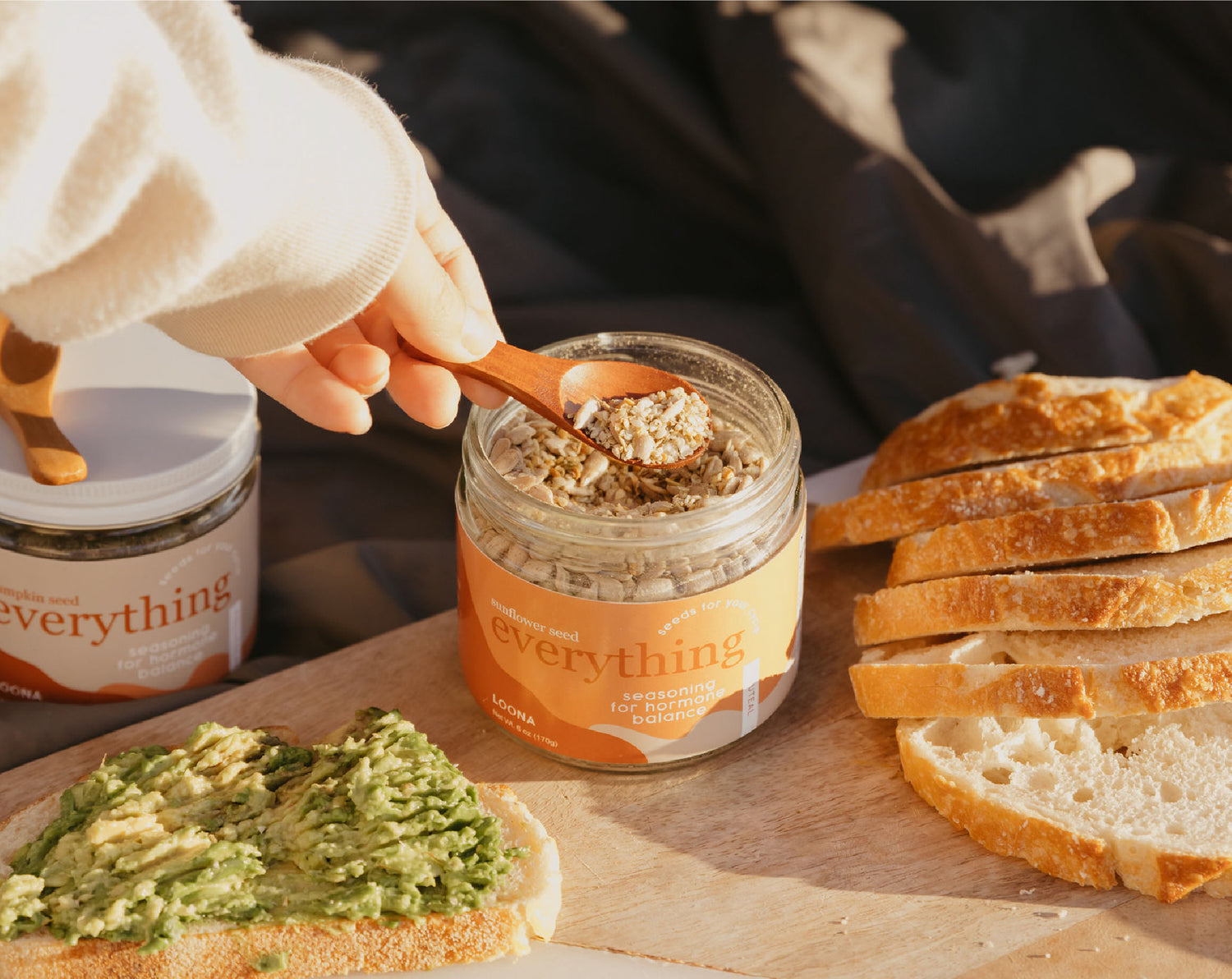 A hand scooping a wooden spoonful of Loona Seeds' Sunflower Seed blend.