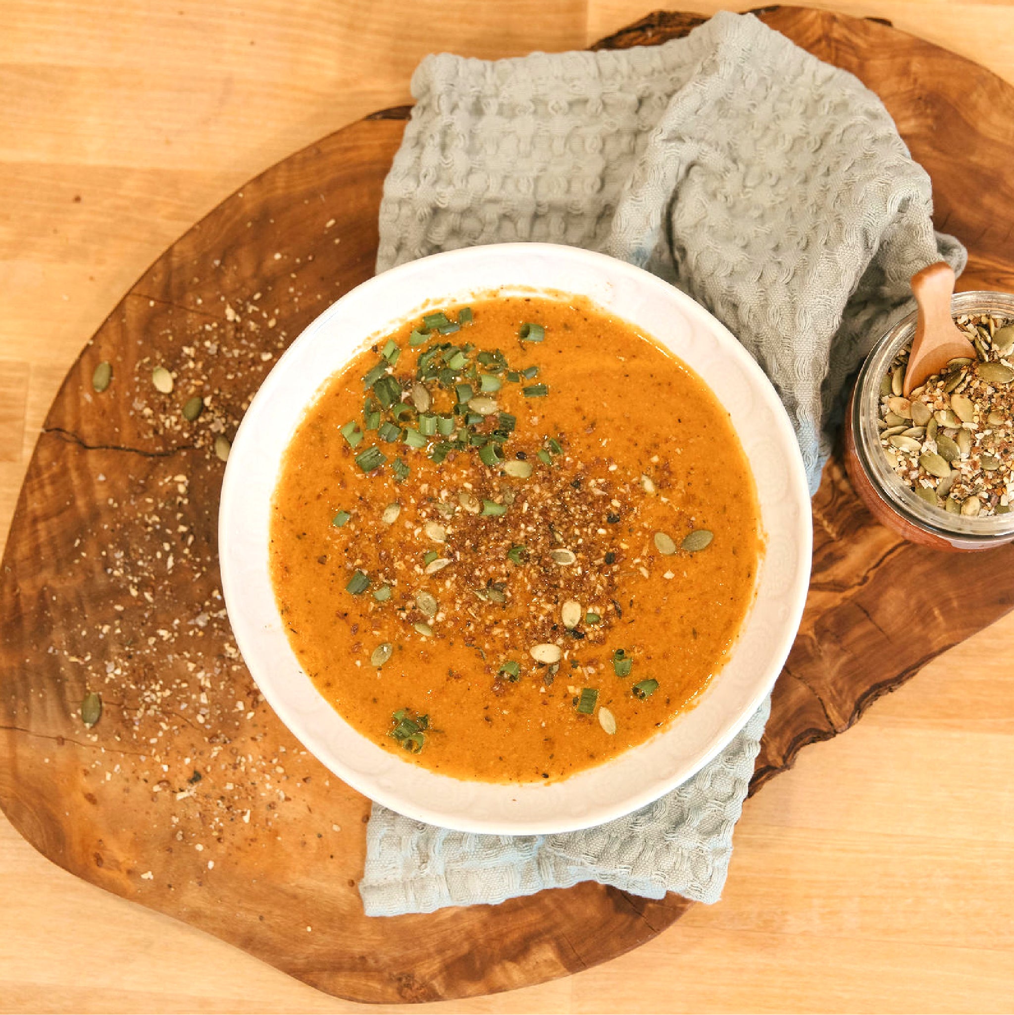 A bowl of soup, sprinkled with seeds, sitting on a wooden table.