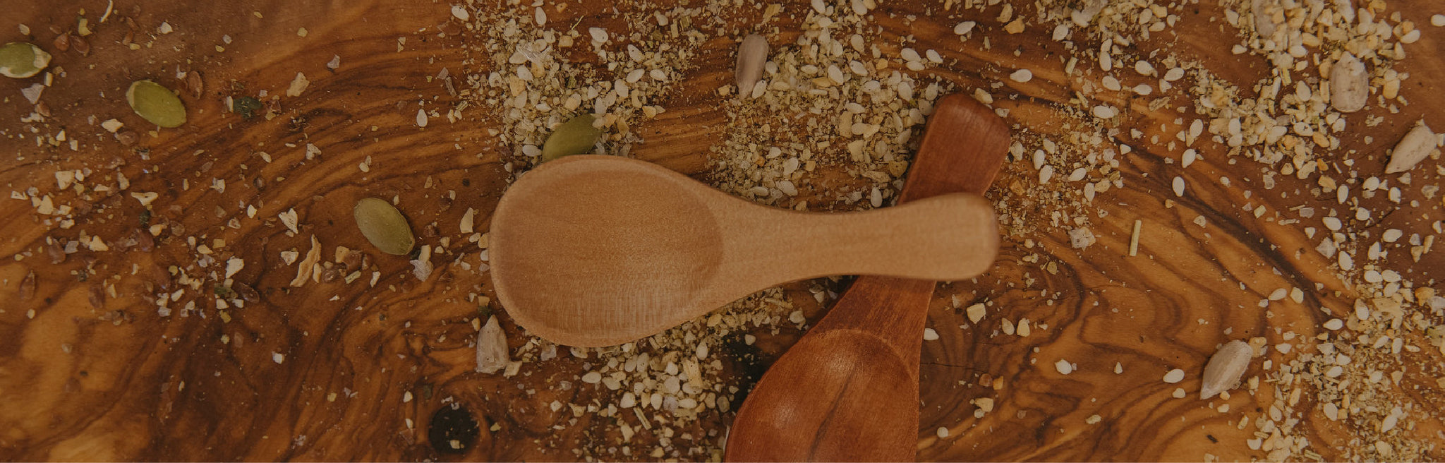 Two crossed wooden spoons, sitting on a wooden table scattered with seeds.