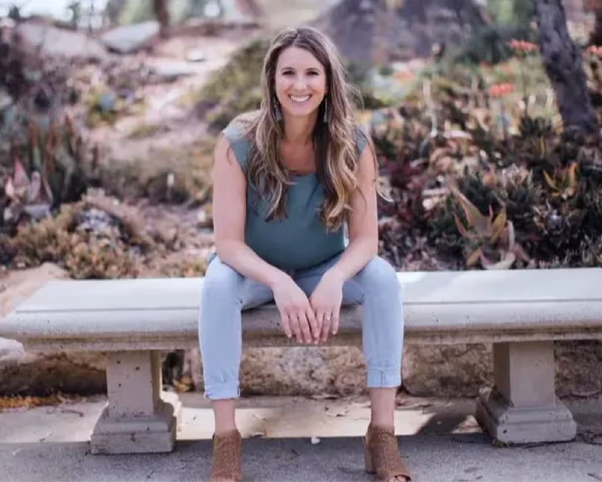 A picture of Dr. Leah Gordon, sitting on a stone bench and smiling into the camera.