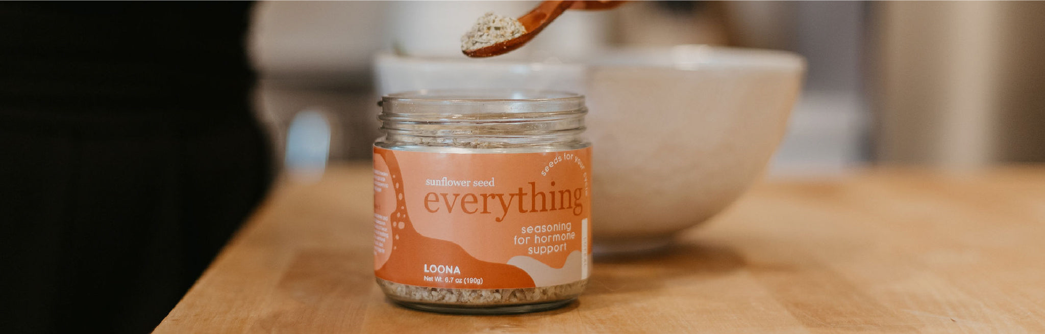 Jar of Loona Seeds' Sunflower Seed blend, sitting on a table with a wooden spoon.