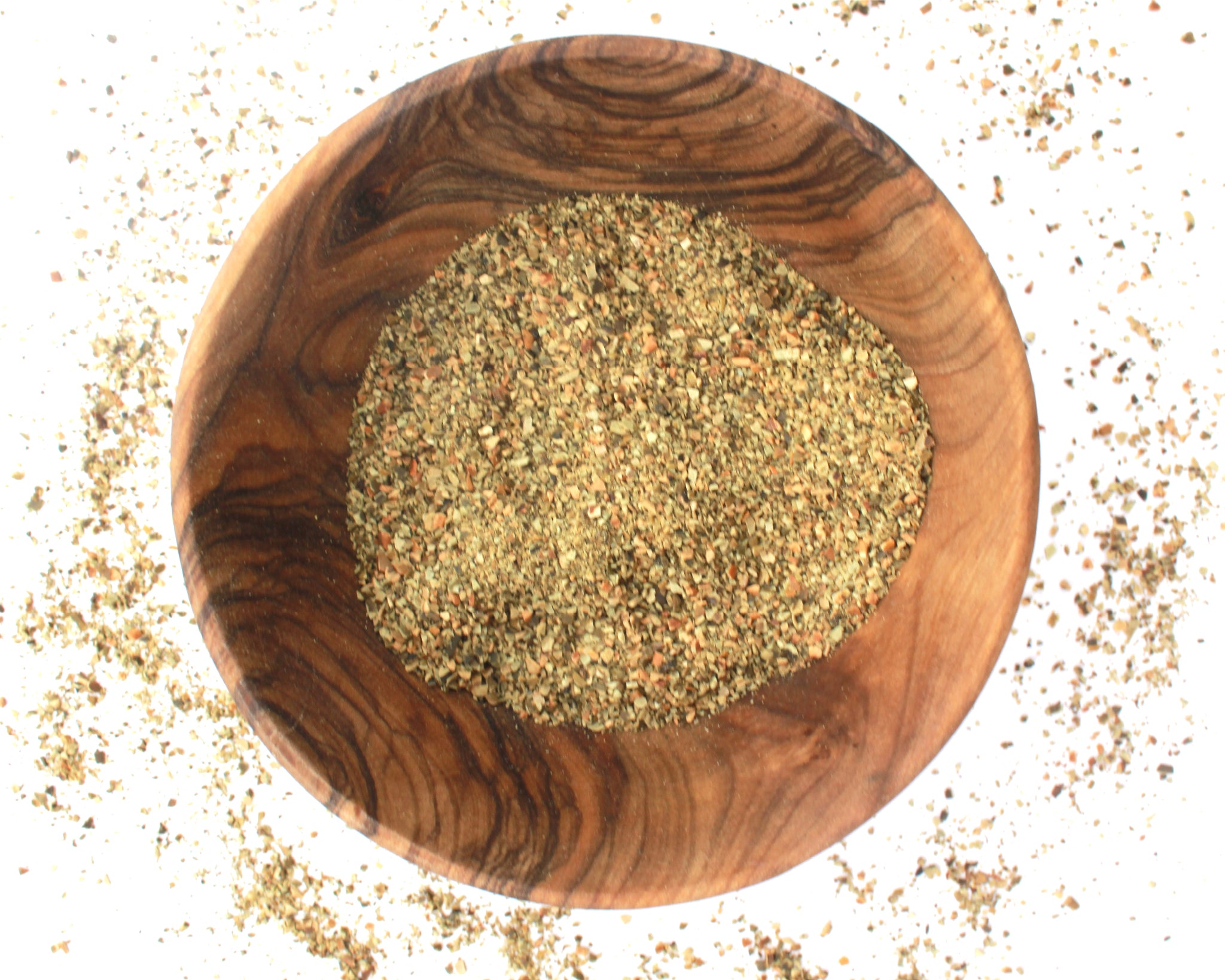 A small wooden bowl filled with sea kelp, on a white background with kelp fragments scattered around it.